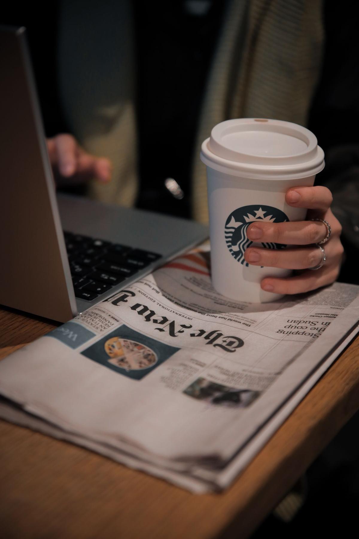 Pembaca menikmati kopi sambil membaca berita di laptop
